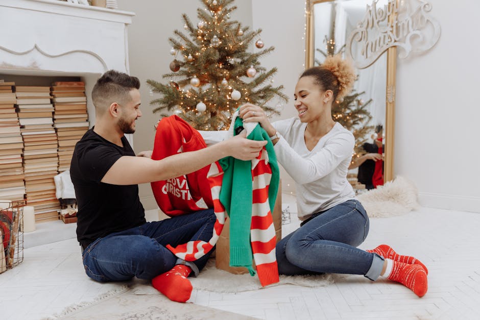 A cheerful couple exchange holiday sweaters near a decorated Christmas tree indoors.